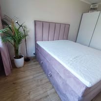 Łóżko tapicerowane w kolorze pudrowego różu w jasnej sypialni